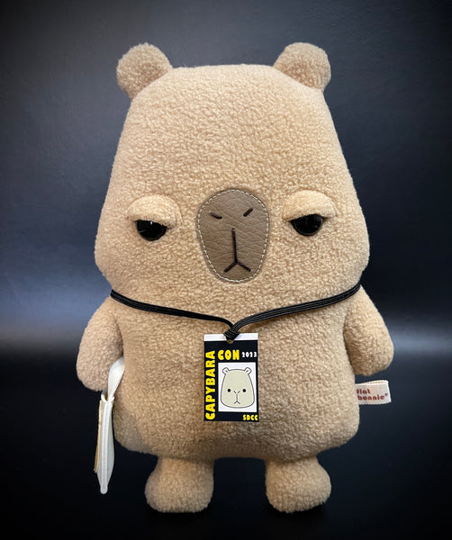 Unimpressed and Judgy looking Capybara plush with event badge and a tote bag accessories - front view