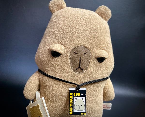 Unimpressed and Judgy looking Capybara plush with event badge and a tote bag accessories